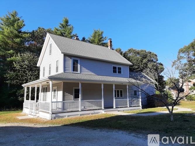 A two-story house with a porch and a tree in front.