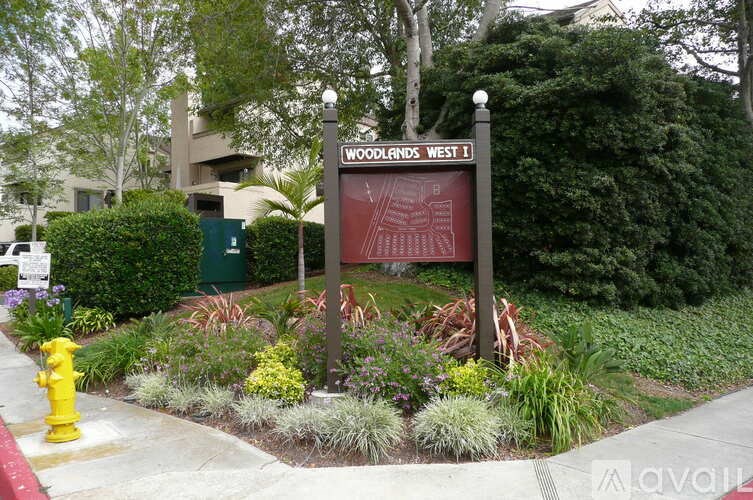 A sign for Woodlands West is in front of a building and a fire hydrant.