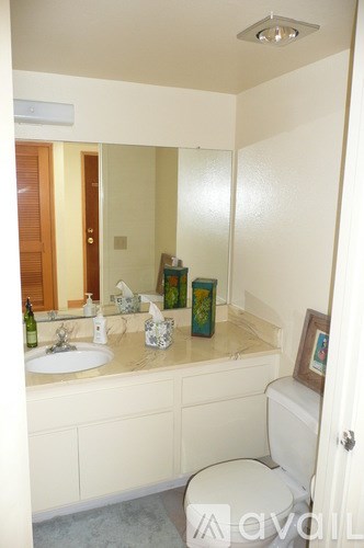 A bathroom with a toilet, sink, mirror and a picture frame.