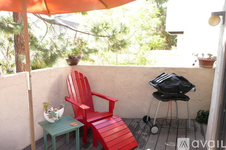 A red chair and a small table with a vase on it are on a balcony.