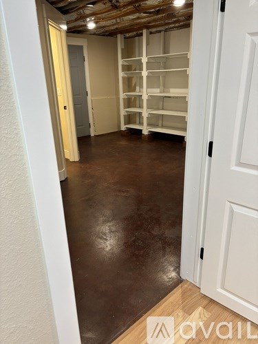 A room with white walls and a brown floor with shelves on the wall.