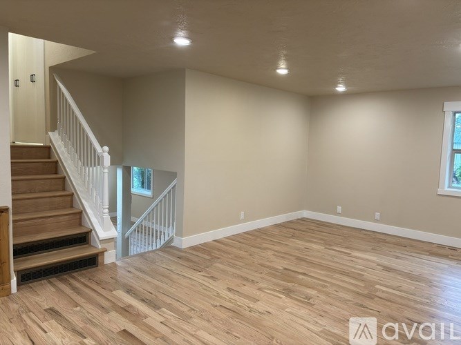 A spacious room with wooden flooring and a staircase leading to another level.