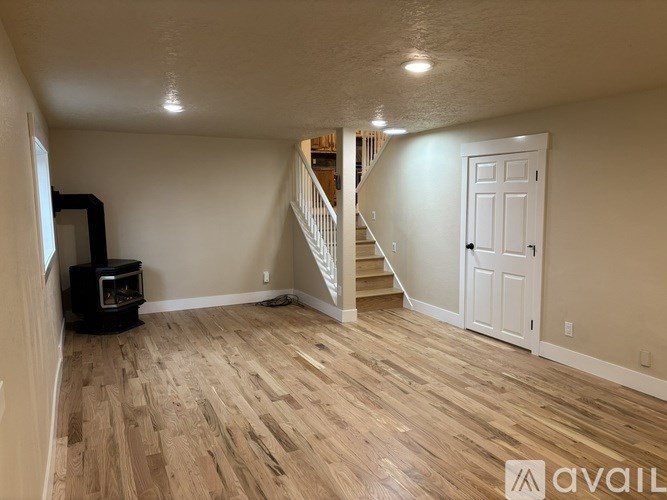 A room with wooden flooring and a staircase in the background.