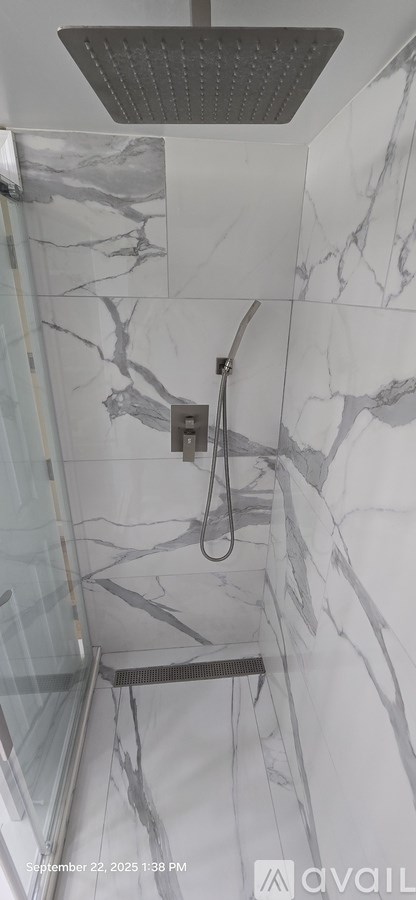 A shower with a marble wall and a metal shower head.