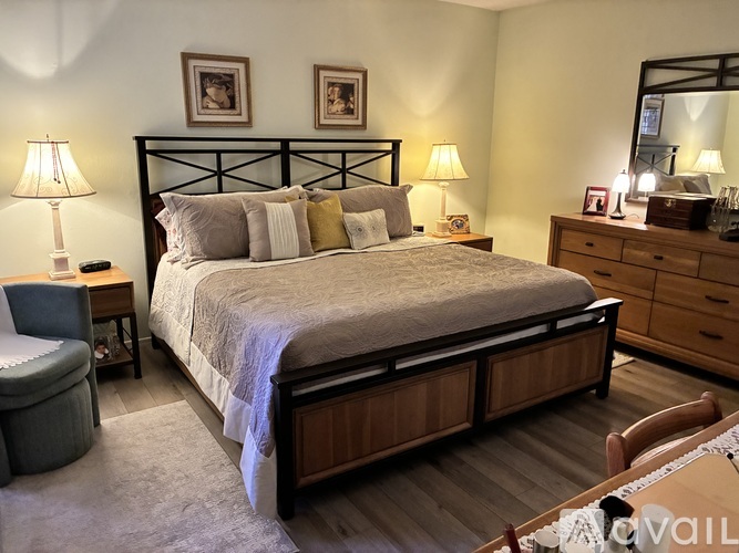 A bedroom with a large bed, a chair, and a nightstand with a lamp.