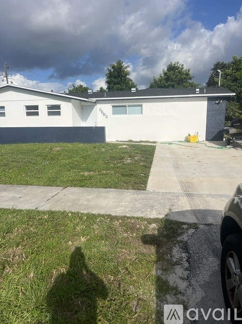 A white house with a grey roof and a black car parked in front.