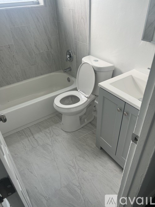 A white toilet is in a bathroom with a white tub and sink.