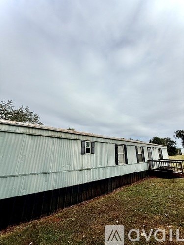 A silver trailer with a small deck and a single window is parked in a grassy area.