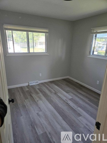 A room with grey flooring and two windows.