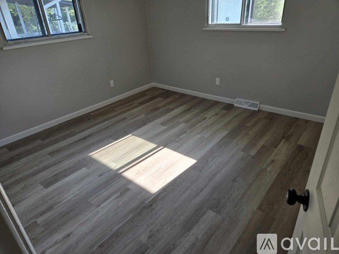 A room with wooden flooring and two windows.
