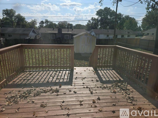 A wooden deck with leaves scattered on it and a house in the background.