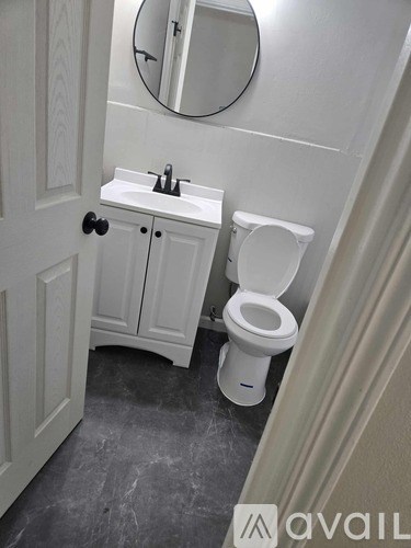 A white toilet in a bathroom with a white cabinet and a round mirror above it.