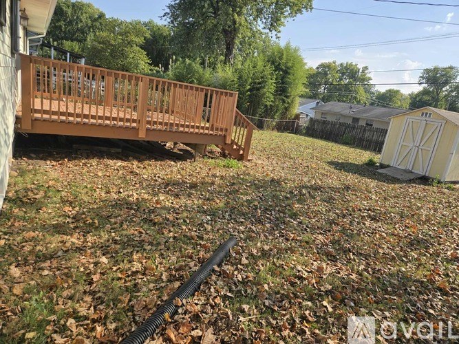 A wooden deck is in the foreground of a yard with a shed in the background.