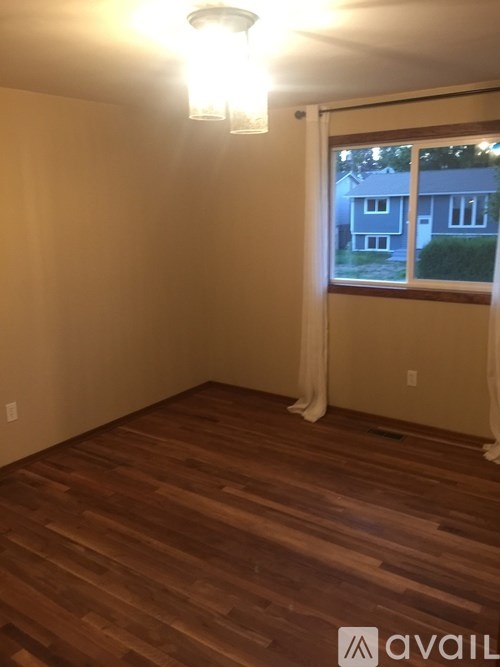 A room with wooden flooring and a window overlooking a house.