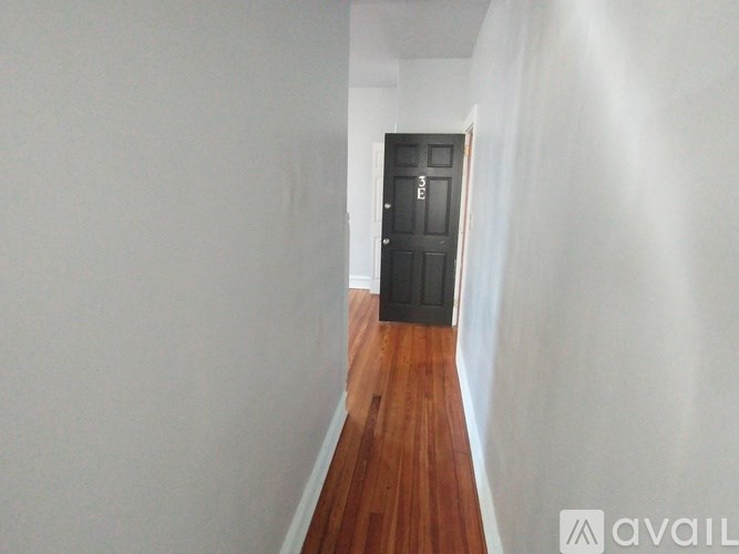 A hallway with a black door and wooden floor.