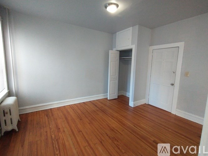 A room with wooden floors and white walls, with a small white cabinet and a door on the right.