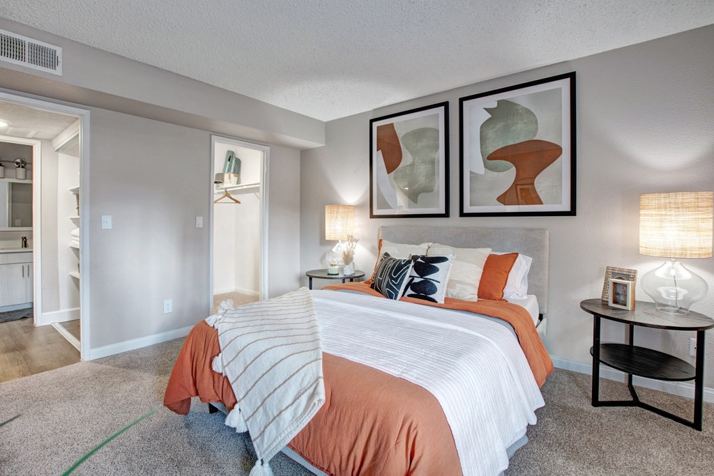 A bedroom with a bed, nightstand, and two framed artworks on the wall.
