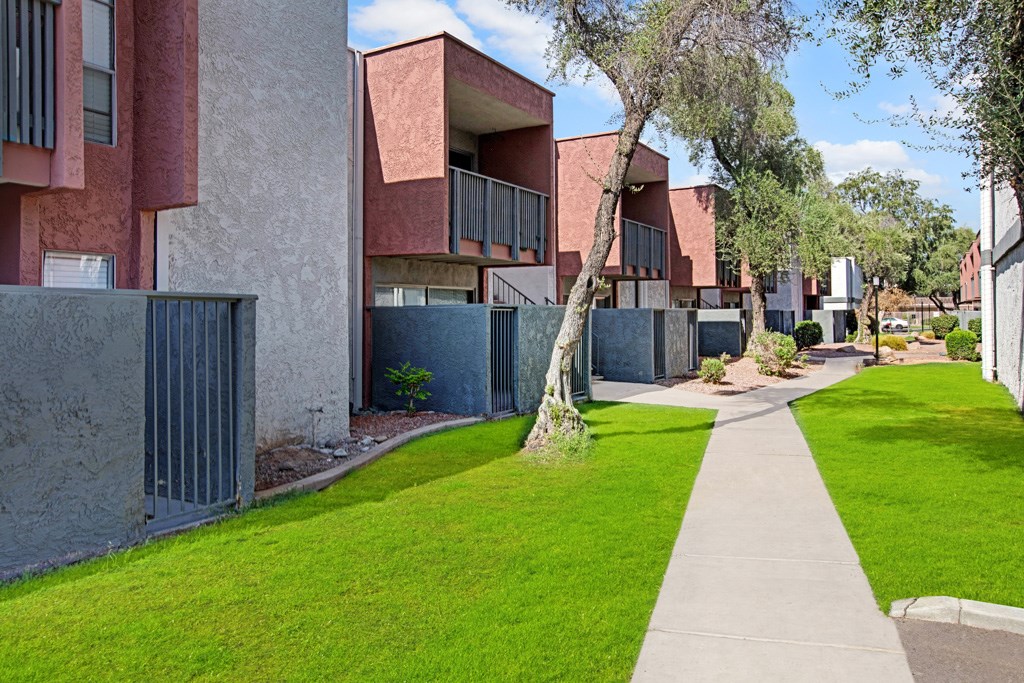 A long concrete walkway leads through a grassy area between two buildings.