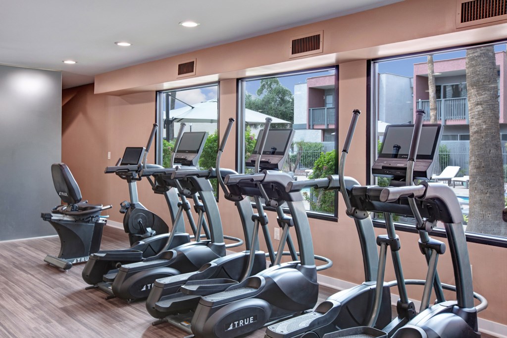 A gym with exercise bikes and a view of apartment buildings outside the window.