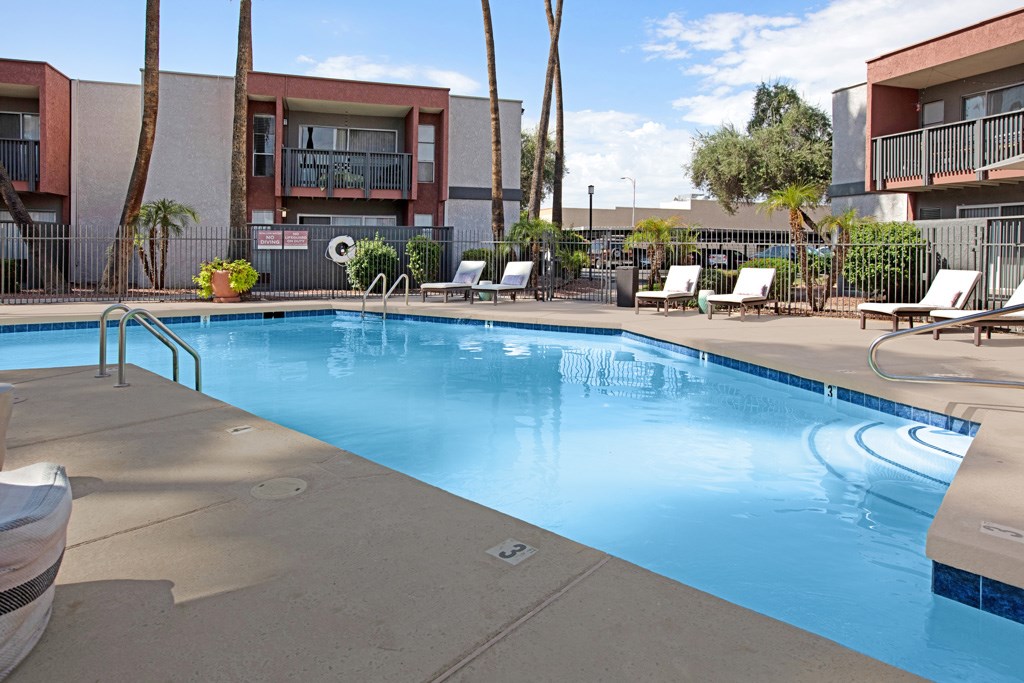 A swimming pool surrounded by lounge chairs and palm trees.