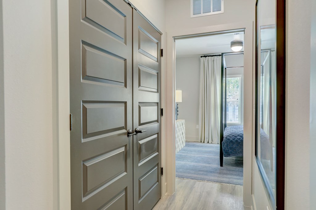 A grey door is open to a room with a bed and a window.