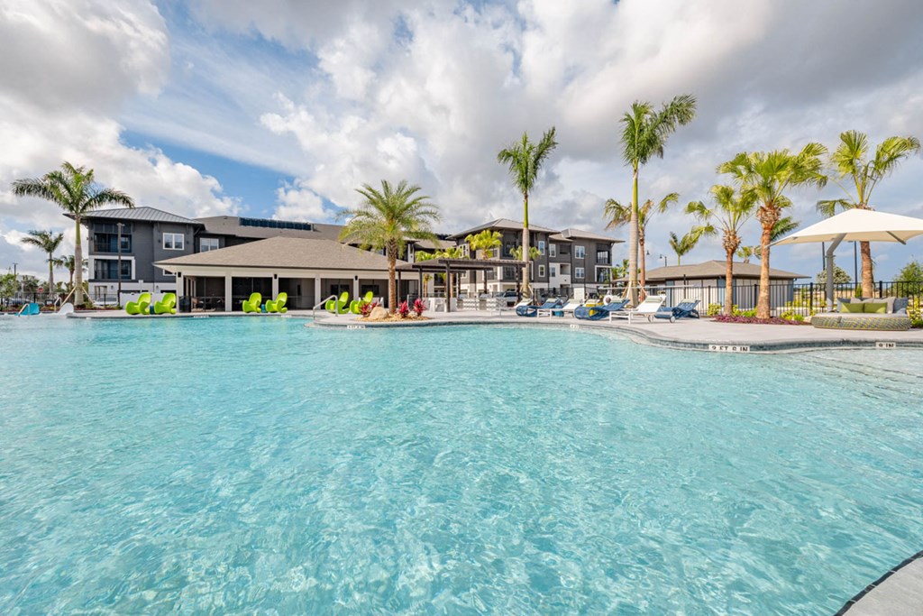 A large swimming pool in front of a resort with palm trees.