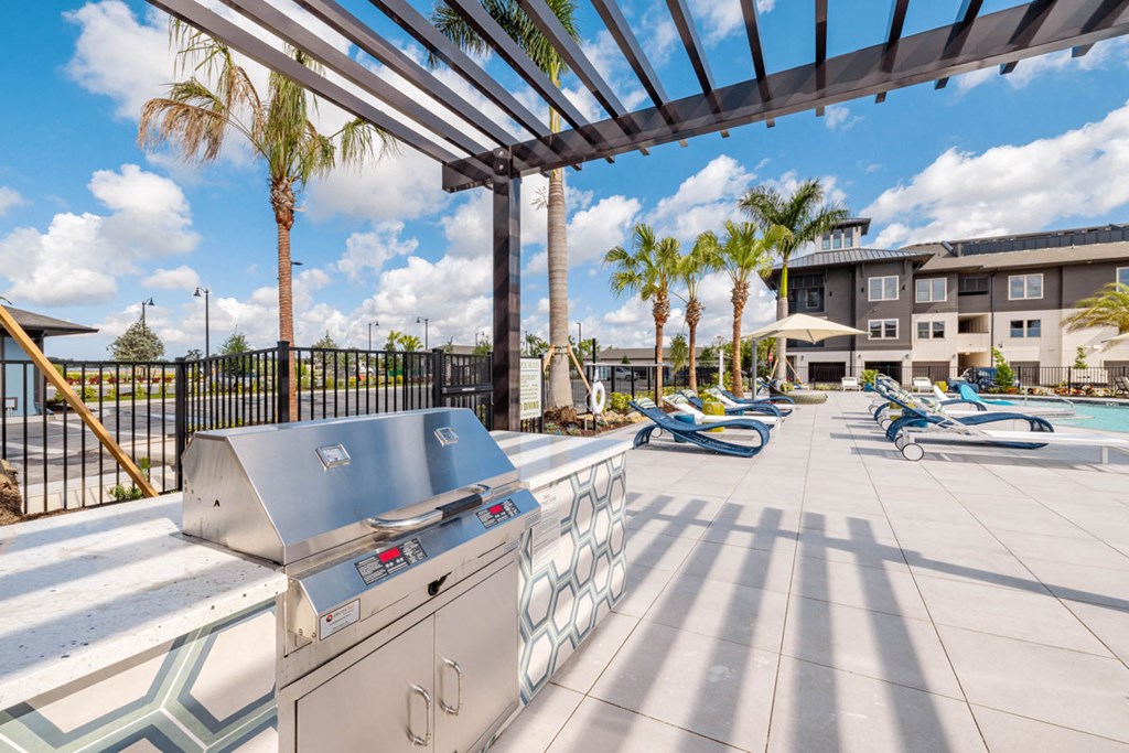 A BBQ grill is on a patio with a pool table and a building in the background.