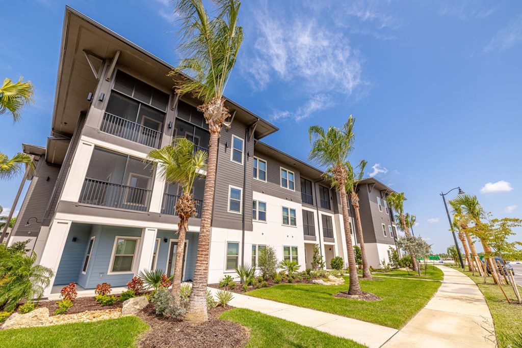 A row of modern townhouses with balconies and palm trees in front.
