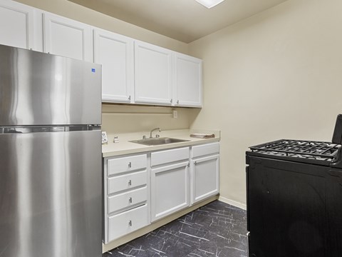 A kitchen with a stainless steel refrigerator, white cabinets, and a black stove top oven.