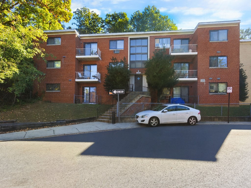 A white car is parked in front of a red brick apartment building.