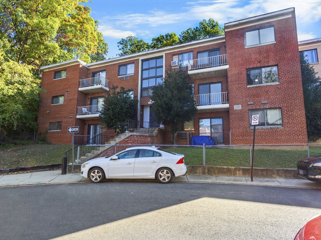 A white car is parked in front of a red brick apartment building.