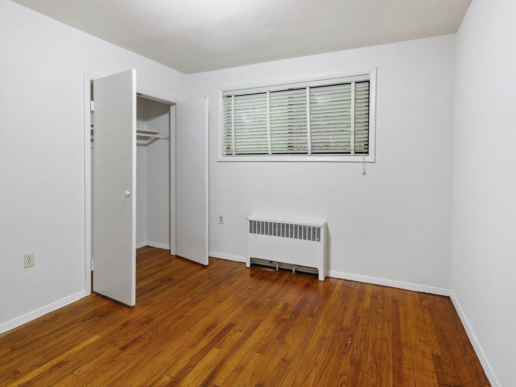 A room with a wood floor and a window with blinds.