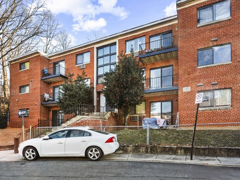 A white car is parked in front of a red brick apartment building.