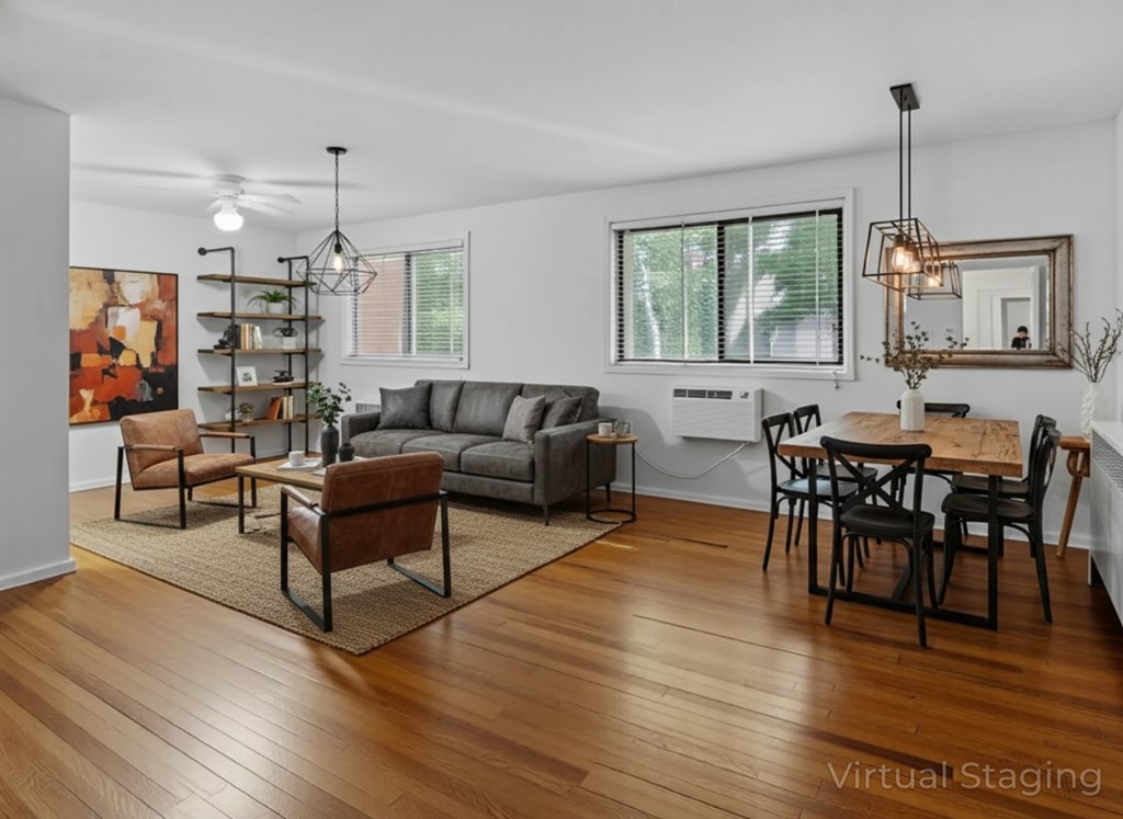 A living room with a grey couch, a brown leather chair, a wooden dining table with chairs, and a rug on the floor.