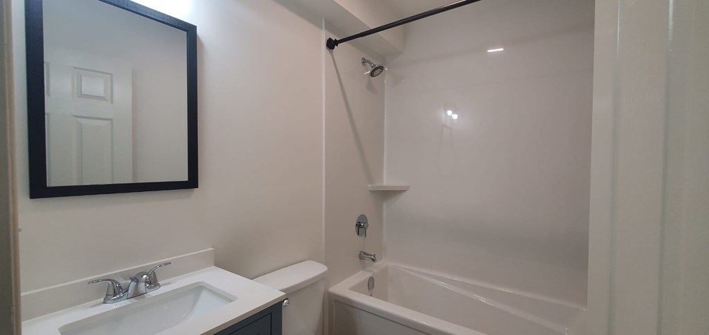 A white bathroom with a sink, mirror, and bathtub.