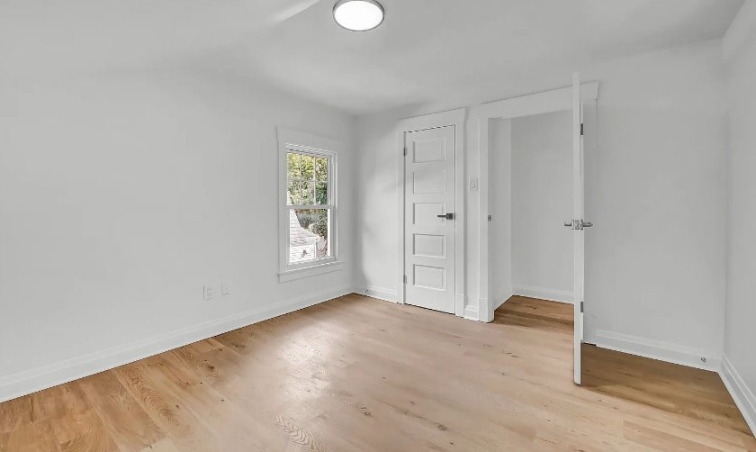 A room with a white door and a window with a view of trees and a house.