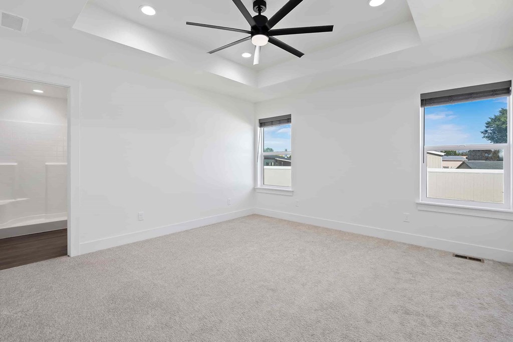 A spacious room with a ceiling fan and two windows.