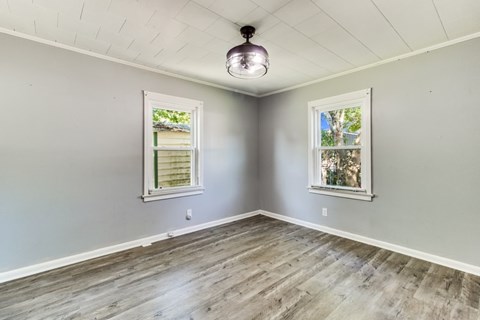 A room with wooden flooring and two windows.