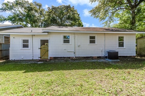 A small white house with a yellow door and a black trash can.