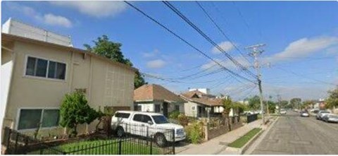 A residential street with houses on both sides and cars parked along the curb.