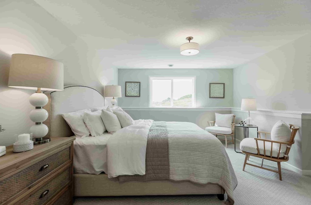 A bedroom with a large bed, a chair, and a window.