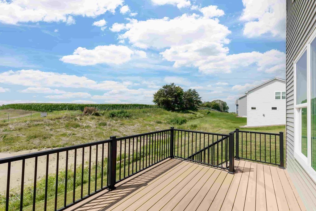 A wooden deck with a black railing overlooks a grassy field.
