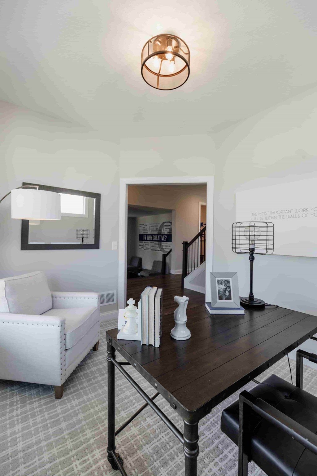 A white chair sits in front of a table with a lamp and picture frame on it.