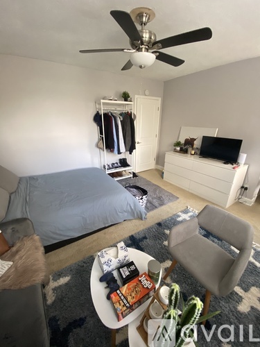 A bedroom with a bed, a chair, a table with snacks, and a ceiling fan.