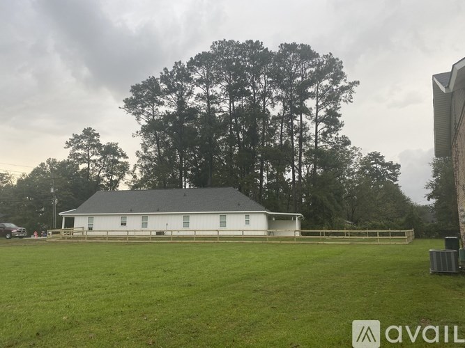 A white house with a grey roof is surrounded by a grassy field and trees.