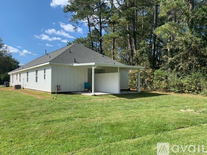 A white house with a black roof is surrounded by green grass and trees.