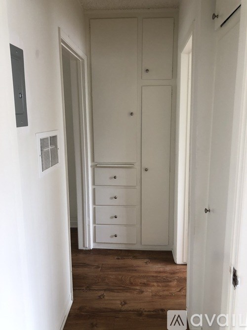 A white hallway with a door on the right and a white cupboard with drawers on the left.