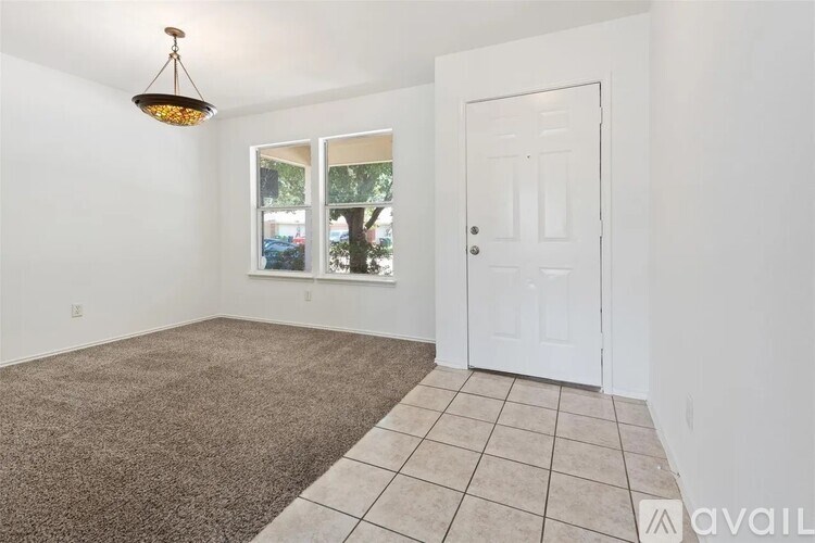 A room with a carpeted floor, a white door, and a window with a view of trees.