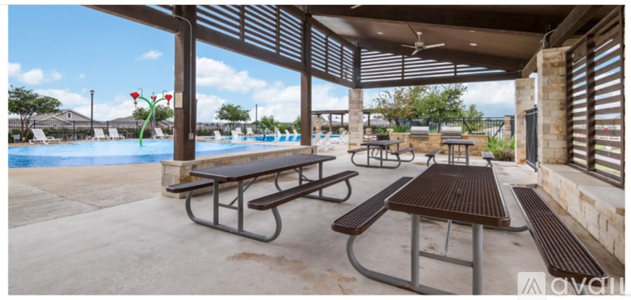 Picnic tables are set up under a pavilion by a pool.