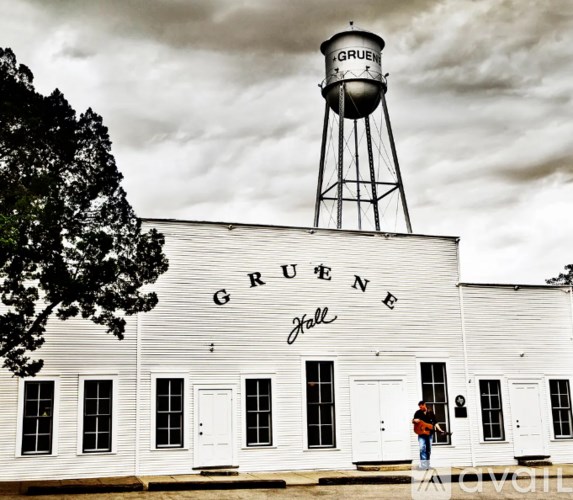 A man is playing guitar in front of a white building with a water tower.